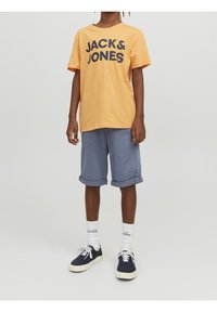 Oranje katoenen t-shirt met "JACK & JONES" in donkerblauw bedrukt, gecombineerd met lichtblauwe opgerolde shorts, witte crew sokken en marineblauwe sneakers.