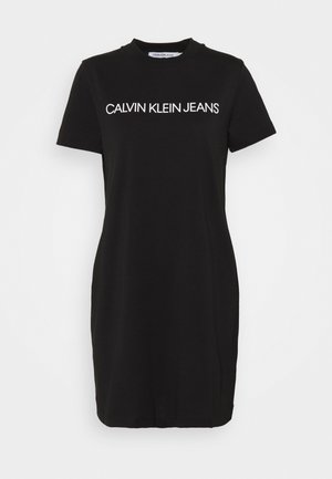 Musta t-paita-mekkoinen lyhythihainen mekko, jossa valkoinen "CALVIN KLEIN JEANS" teksti keskellä rintaa ja pyöreä pääntie.