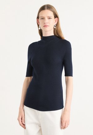 Mørkeblå kortermet strikket topp med høy hals, med ribbestruktur og tettsittende fasong. Merker av sømdetaljer på sidene.