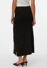 Jupe maxi en maille côtelée sombre avec une taille ajustée, dotée d'une rangée de boutons sur un côté, associée à des talons aiguilles.