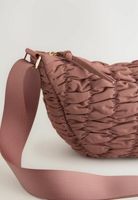 Pouch-stijl tas van een textuur met geplooide stof in stofroze, met een soepele ritsluiting en een brede, platte schouderband. Gouden hardware accenten.