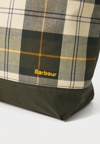 Torba na ramię w kratkę w kolorach beżowym, zielonym i granatowym z pomarańczowym akcentem. Zawiera logo Barbour w kolorze żółtym na ciemnozielonym tle.