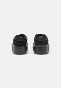 Pár černých semišových tenisek Converse All Star nízkého střihu z pohledu zezadu s černou gumovou podrážkou a logem hvězdy na patních dílech.