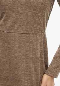 Robe marron en tricot côtelé présentant une surface texturée, des manches longues et une taille empire. Silhouette simple et ajustée sans détails supplémentaires.