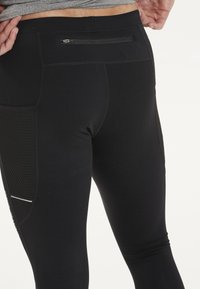Zwarte sportleggingen met een zijvak van mesh, een ritszak aan de achterkant en gestructureerde naden voor een aansluitende pasvorm.