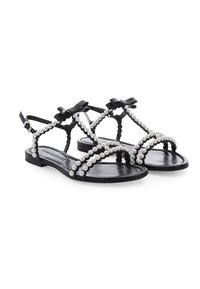 Schwarze flache Sandalen mit mit Perlen besetzten Riemen und kleinen schwarzen Schleifen an den Knöchelriemen, auf weißem Hintergrund präsentiert.