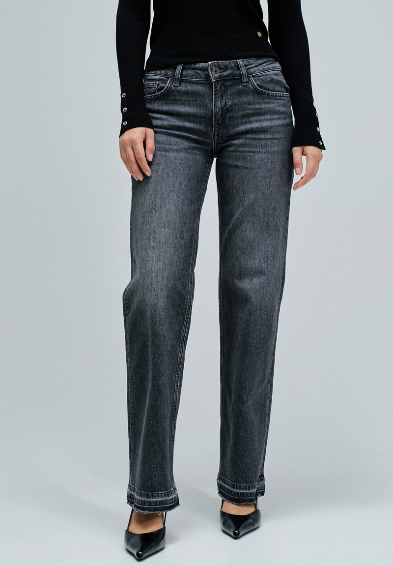 Jeans de mezclilla gris con un ajuste relajado, que cuentan con un diseño clásico de cinco bolsillos, con un sutil desgaste y detalles en el dobladillo deshilachado, combinados con tacones negros.