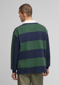Long-sleeve polo shirt in alternating green and navy stripes, with a white collar. Soft cotton material and relaxed fit.
