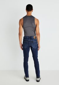 Grå ermeløs tanktop og mørkeblå denimjeans med et lærlabel fra Lee på baklomma, med slank passform og minimalistisk design.