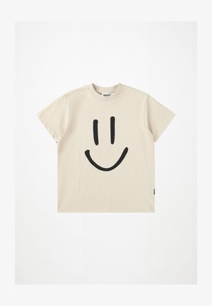 Beige t-paita lyhyillä hihoilla, jossa on suuri musta hymyilevä naama -grafiikka edessä ja pieni musta brändilippu sivussa.