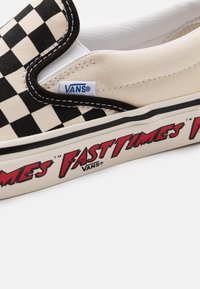 Chaussure à enfiler à carreaux noir et blanc, en toile, avec une semelle en caoutchouc portant l'inscription « Fast Times » en lettres rouges sur le côté.