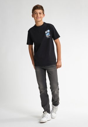 T-shirt nera in cotone con una stampa grafica blu e bianca sul davanti, abbinata a jeans grigi e sneakers bianche.