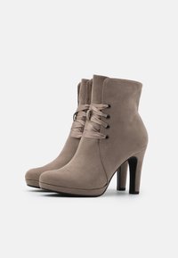 Botines de ante beige con un acabado suave, punta redonda y tacón stiletto alto. Cuentan con cordones de satén y ojales de metal para el cierre.