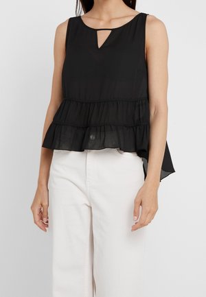 Schwarze ärmellose Bluse mit abgestuften Volants am Saum und kleinem V-förmigem Schlitz am Ausschnitt, getragen zu hoch taillierten weißen Hosen.