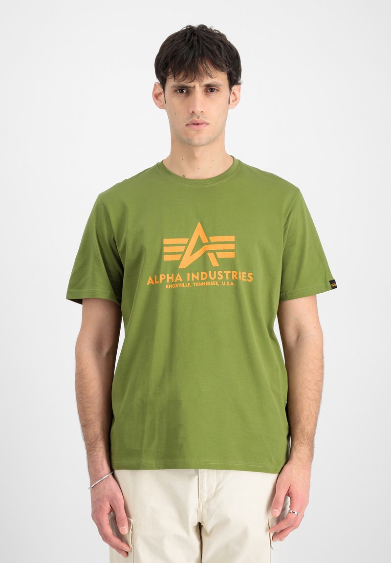 Grøn bomulds T-shirt med et orange logo, der har stjerne- og stribedesign. Korte ærmer, rund hals, afslappet pasform og ensartet tekstur.