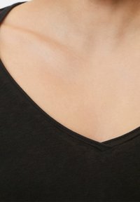 Close-up of a person’s upper chest and neck wearing a black V-neck shirt with smooth, light skin.