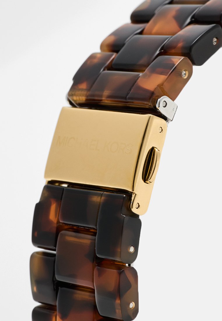 Bracelet Michael Kors présentant un design chunky en écaille de tortue marron et noir avec un fermoir doré et un détail gravé du logo.