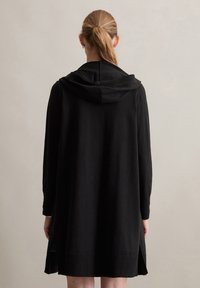 Schwarzes Kapuzenkleid mit langen Ärmeln, gestrickter Textur, seitlichen Schlitzen und lockerer Passform. Einfaches Design ohne sichtbare Muster oder Akzente.