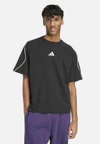 Schwarzes Baumwoll-T-Shirt mit kurzen Ärmeln, rundem Ausschnitt und weißem Adidas-Logo auf der Brust. Mit weißer Paspelierung entlang der Schultern.