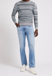 Gestreifter Pullover in Türkis, Grau und Schwarz, kombiniert mit hellblauen Jeans und weißen Sneakers. Der Pullover hat einen gerippten Halsausschnitt und Saum.