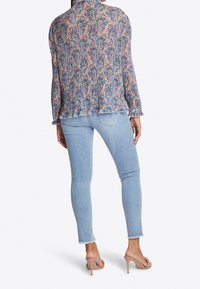 Blusa semitranslúcida con estampado floral, de mangas largas y dobladillo volantero; combinada con jeans ajustados azul claro y zapatillas de tacón en color nude.