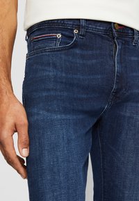 Modré džíny z denimu s úzkým střihem, pěticípým designem kapes a zlatými kovovými detaily. Tkanina má hladkou strukturu s jemným vyblednutím.