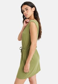 Vestido sin mangas de color verde oliva hecho de una tela suave, que cuenta con una cintura ajustable y un corte relajado, con una ligera forma de A.
