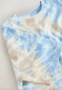 Korte mouwen T-shirt met ronde hals in blauw en beige tie-dye patroon, plat uitgespreid op een witte ondergrond.