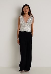 Top od šljaštećih detalja s dubokim V-izrezom, uparen s crnim hlačama visokog struka. Top sadrži iridescentne šljokice koje stvaraju teksturirani izgled.