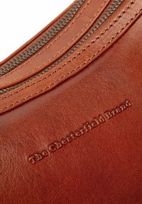 Borsa a mano in pelle marrone, caratterizzata da una texture liscia, forma circolare, cuciture a contrasto e una cerniera con logo del marchio inciso.