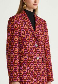 Blazer con motivo colorato caratterizzato da audaci disegni circolari in rosso, arancione e rosa, doppiopetto con bottoni argentati e tasche frontali.