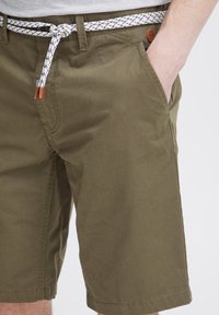 Olivgrüne Shorts aus Baumwolle, mit einem gewebten weißen und marineblauen Gürtel, seitlichen Taschen und einer schlichten Textur mit einem kleinen Lederakzent.
