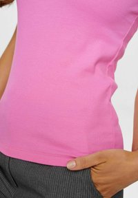 Dopasowany różowy top na ramiączkach z prążkowanej tkaniny, wykonany z rozciągliwego materiału, o gładkiej teksturze i zaokrąglonym dole, w zestawie z szarymi spodniami w paski.