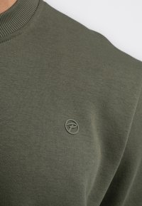 Olijfgroene sweatshirt gemaakt van zachte stof met een geribbelde ronde hals en een klein, geperst logo op de borst. Glad textuur, casual ontwerp.