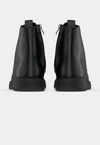 Paire de bottines en cuir noir avec fermetures éclair latérales, vues de dos sur un fond clair uni.