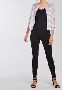 Chaqueta texturizada gris claro con rayas horizontales, top negro sin mangas, pantalones negros ajustados y tacones negros con tiras. Diseño simple y contemporáneo.