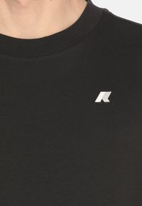 T-shirt in cotone nero con colletto girocollo, caratterizzata da un piccolo logo argento sul lato sinistro. Tessuto liscio, senza motivi visibili.