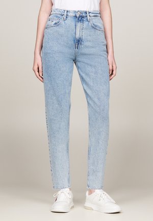 Person trägt hoch taillierte hellblaue Jeans mit geradem Bein, Knopf und Reißverschluss, kombiniert mit weißen Sneakers und einem weißen Top.