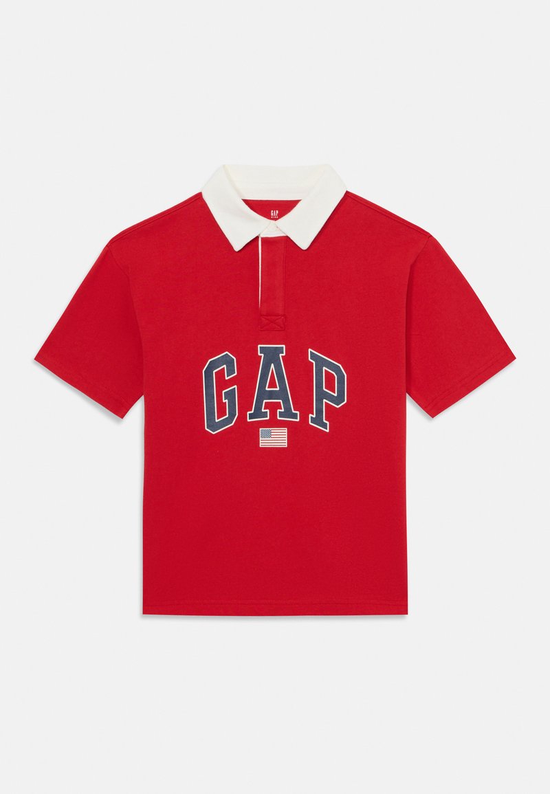 Rdeča polo majica iz bombaža z belim ovratnikom. Na sprednji strani je logo "GAP" v mornarsko modri barvi, pod njim pa je majhna ameriška zastava. Kratki rokavi.