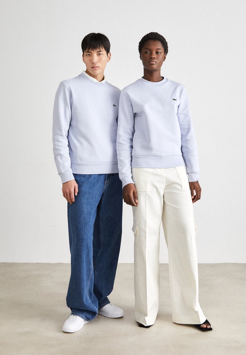 Lichtpaarse sweatshirts met ronde hals, gecombineerd met spijkerbroek en witte cargopantalons, met een logo-detail op de linkerborst.