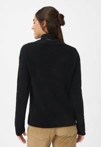 Maglione a maglia nera con maniche lunghe, scollatura rotonda e una texture morbida. Indossato sopra un top nero, abbinato a pantaloni in velluto a coste marrone chiaro.
