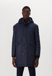 Navy puffer jacket with a hood, featuring a front button closure, two side pockets, and a textured, water-resistant fabric.