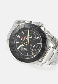 Edelstahlarmbanduhr mit schwarzem Zifferblatt, goldenen Akzenten, Chronographen-Subzifferblättern und einer strukturierten Lünette, ausgestattet mit einem silbernen Gliederarmband.