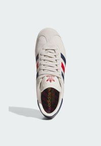 Adidas sneaker with a cream suede upper, navy and red stripes, rounded toe, lace-up front, and a patterned insole featuring the brand logo.