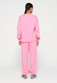 Sudadera de algodón rosa y pantalones deportivos a juego con ajuste relajado. Textura suave, mangas largas y tobillos con puños. Diseño casual y uniforme.