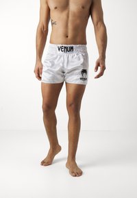 White satin shorts with an elastic waistband, featuring a black "VENUM" logo on the front and a black graphic detail. Elasticated for comfort.