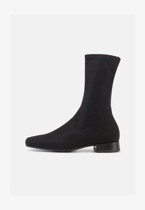 Fekete bokacsizma sima, rugalmas anyag felsőrésszel és alacsony, rétegezett sarokkal. Jellemzői a hegyes orr és a varrás nélküli kialakítás.