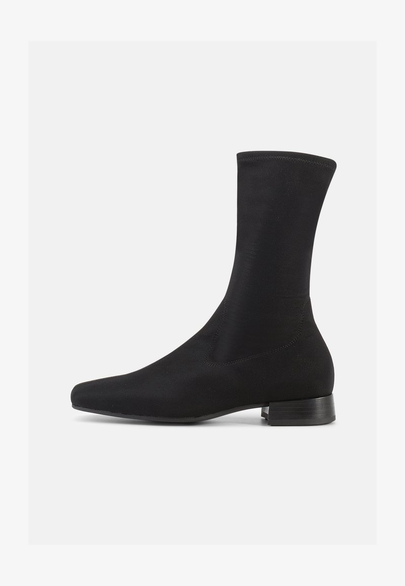 Černá kotníková bota s hladkým, pružným textilním svrškem a nízkým, vrstveným podpatkem. Má špičatou špičku a bezešvý design.