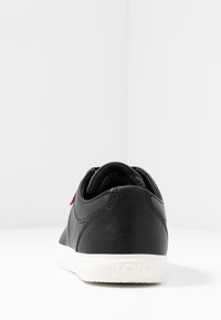 Sneaker in pelle sintetica nera con suola in gomma bianca, caratterizzato da una superficie texturizzata e un piccolo logo rosso Levi's sul tallone.
