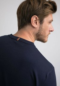 Pull en ribbed bleu marine avec col rond, comportant une petite étiquette multicolore à l'arrière, fabriqué dans un tissu doux.